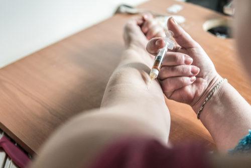 person using a syringe to insert drugs into their veins