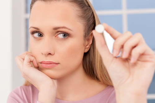 woman holding up a pill questioning to take it or not