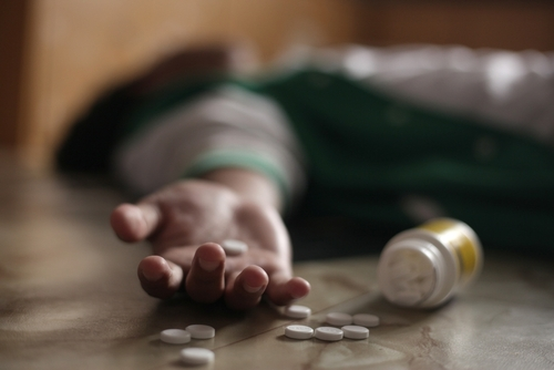 man laying on floor after overdosing on pills with pills in his hand