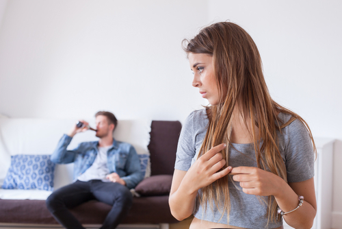 woman looks uneasy while man drinks in the background