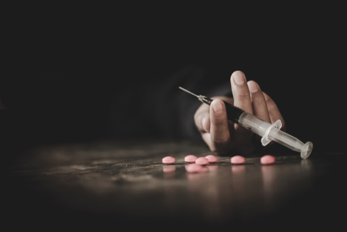 hand holding a syringe with pills on floor after taking fentanyl