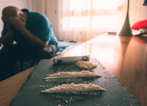 cocaine in lines on table with man sitting on couch with his head in his hands