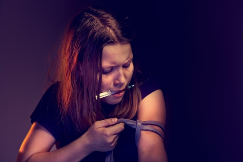 woman putting a tourniquet on her arm so she can shoot meth 